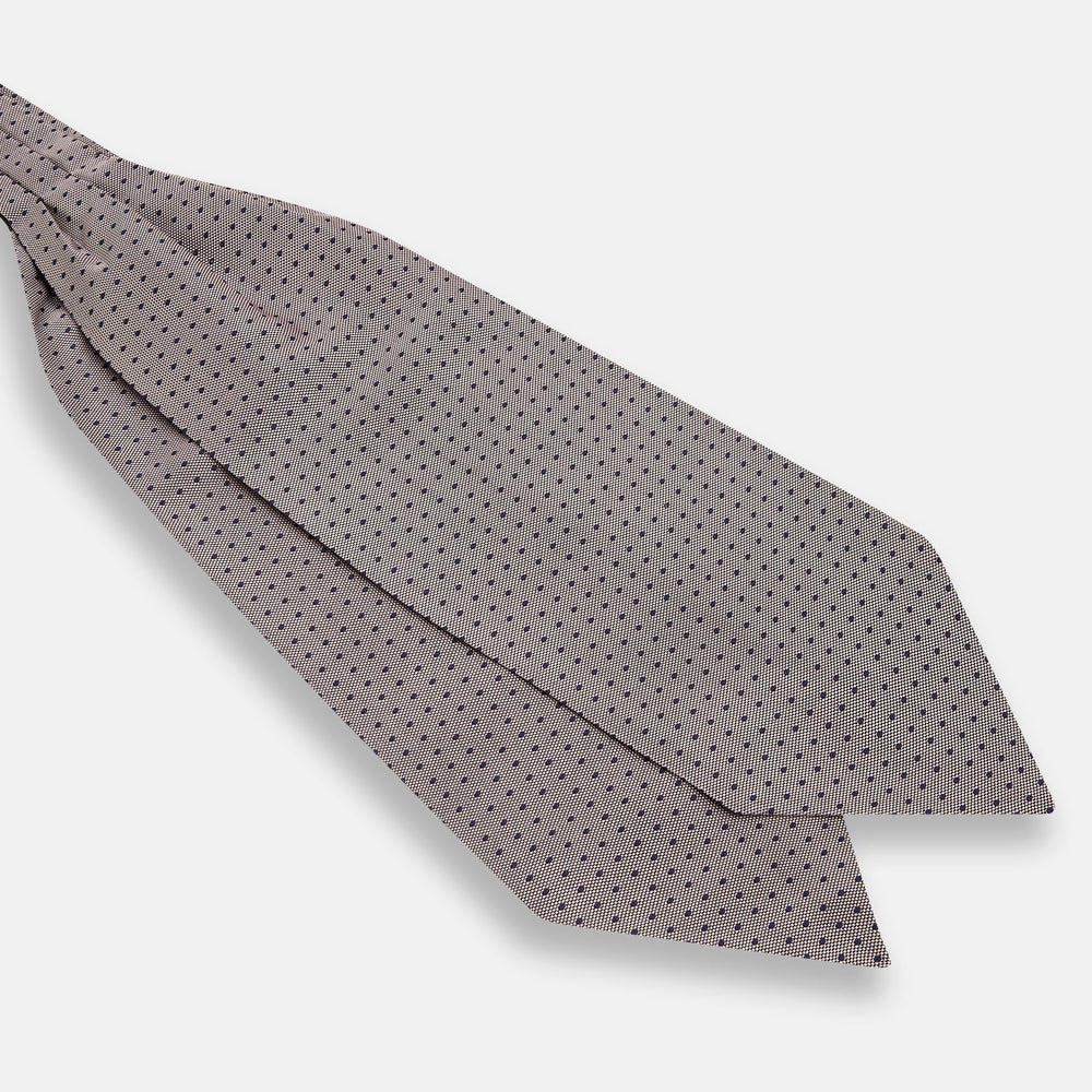 A folded, light-colored pocket square with small dark dots is displayed on a white background. Neatly arranged in a pointed fold, it pairs perfectly with the Turnbull & Asser Lilac and Navy Micro Dot Silk Cravat for an elegant look.