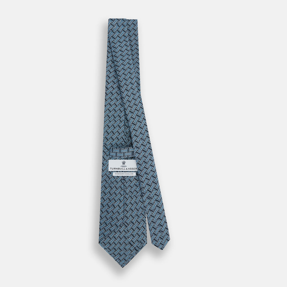A rolled-up Turnbull & Asser Pale Blue and Navy Weave-Patterned Printed Silk Tie is shown against a white background.