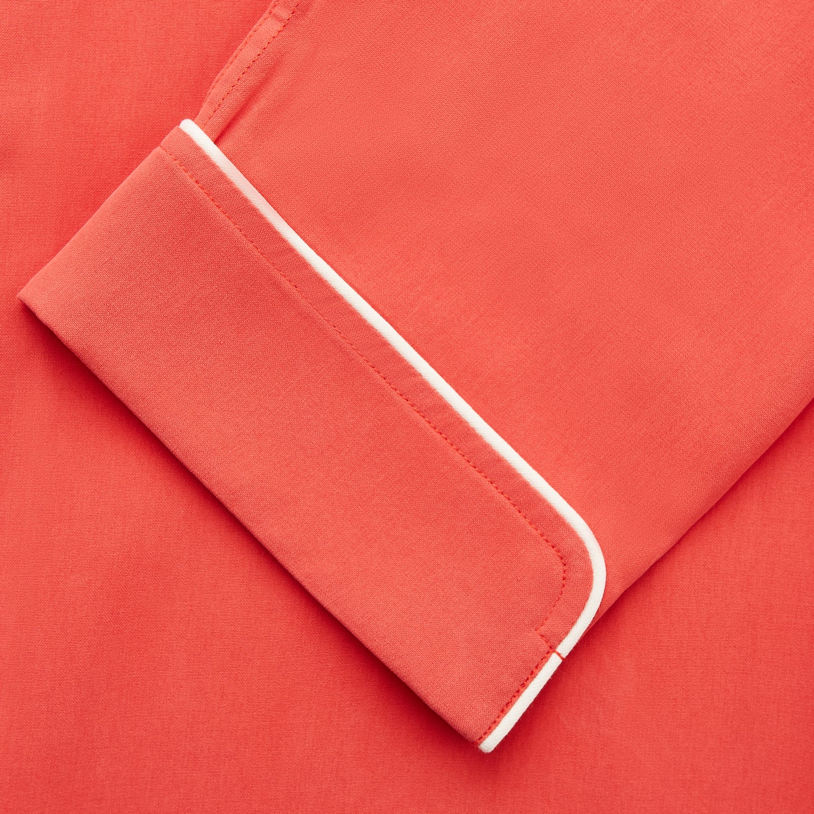 View 3 of product The Turnbull & Asser Women's Coral Pink Silk Thelma Pyjama Set features a long-sleeve button-up top with two front pockets and matching drawstring pants, shown on a white background.