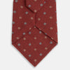 View 3 of product A Turnbull & Asser Red Motif Silk Tie featuring small blue and yellow floral designs with brown geometric shapes is displayed rolled up on a plain white background.