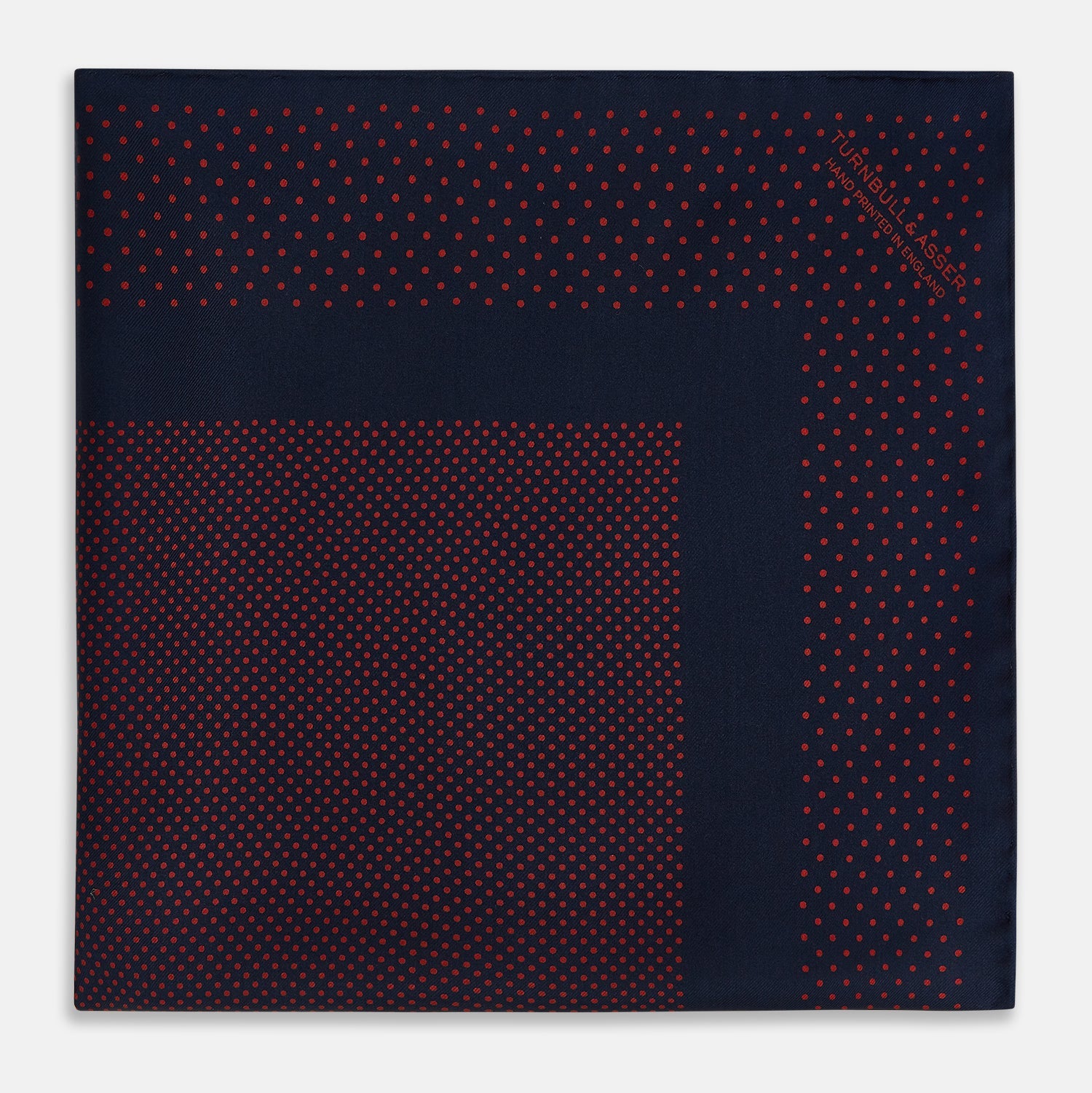 View 3 of product The Turnbull & Asser Navy and Red Dot Silk Pocket Square features a dark navy blue base with small red polka dots on the border and inner pattern, all handmade and neatly folded.