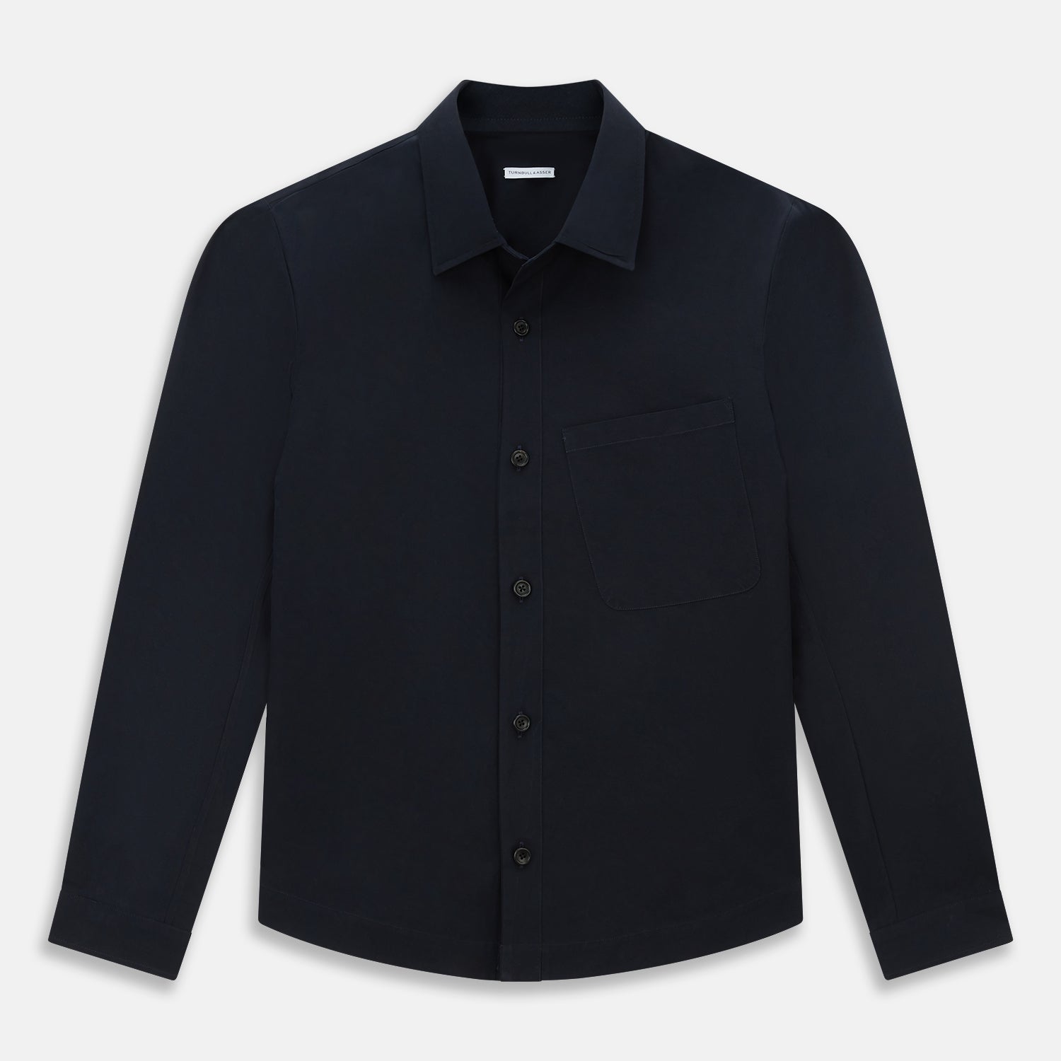 View 1 of product The Midnight Blue Hyde Overshirt by Turnbull & Asser is a plain, long-sleeve shirt in dark navy sanforised cotton with a single chest pocket, spread collar, and black buttons, shown laid flat on a white background.
