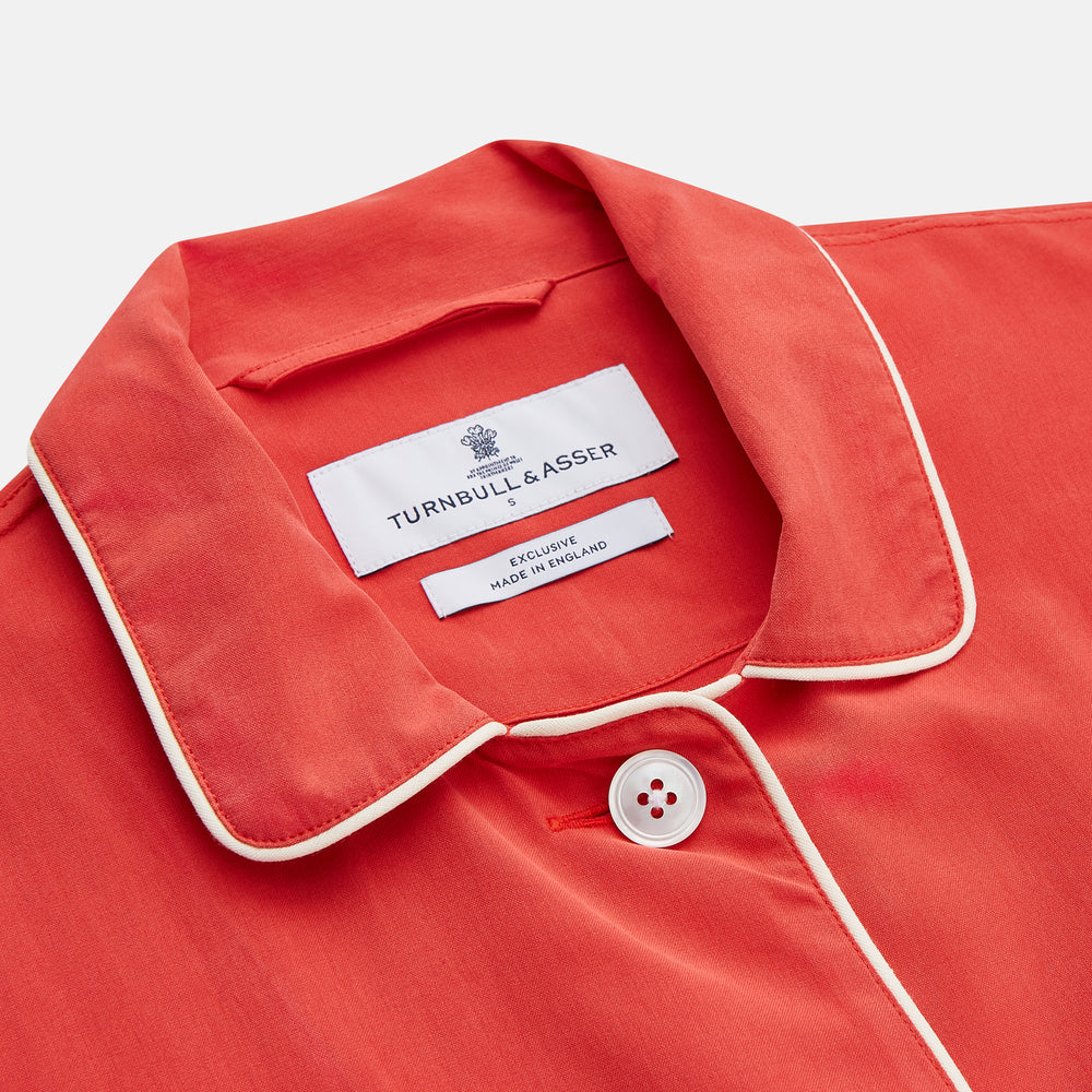The Turnbull & Asser Women's Coral Pink Silk Thelma Pyjama Set features a long-sleeve button-up top with two front pockets and matching drawstring pants, shown on a white background.