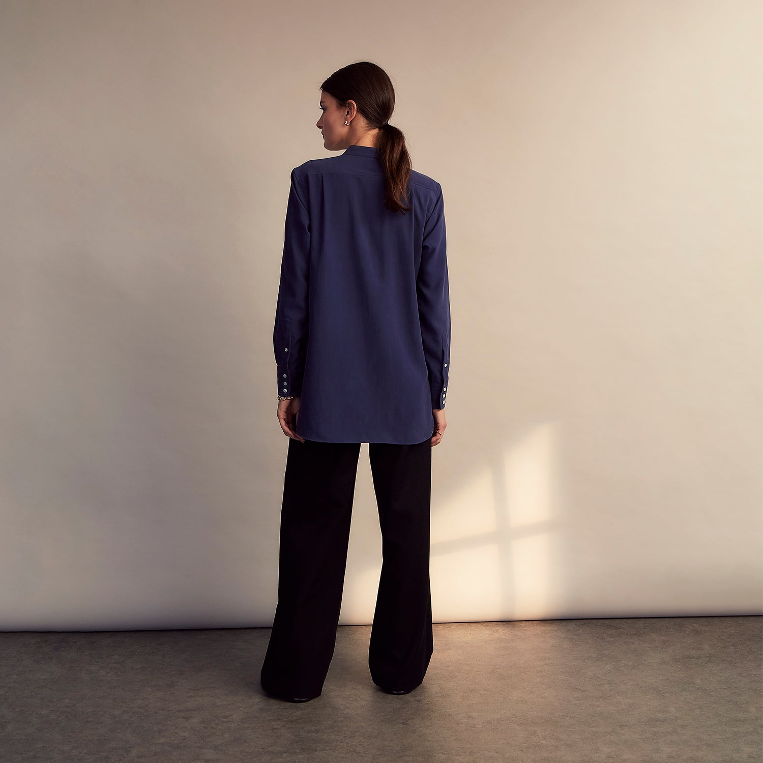 View 7 of product The Turnbull & Asser Blue Soft-touch Silk Lauren Shirt is a navy, long-sleeve button-up with an Igret stand collar, white buttons, curved hem, relaxed fit, and elongated body for a modern look, shown laid flat on a white background.