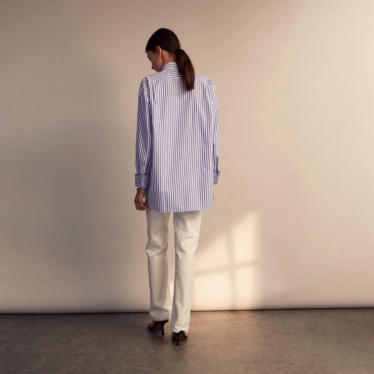 View 10 of product The Turnbull & Asser Pale Blue Candy Stripe Cotton Marlene Shirt is an oversized women's collared shirt with long sleeves, buttoned cuffs, and vertical blue and white stripes, shown laid flat on a white background.