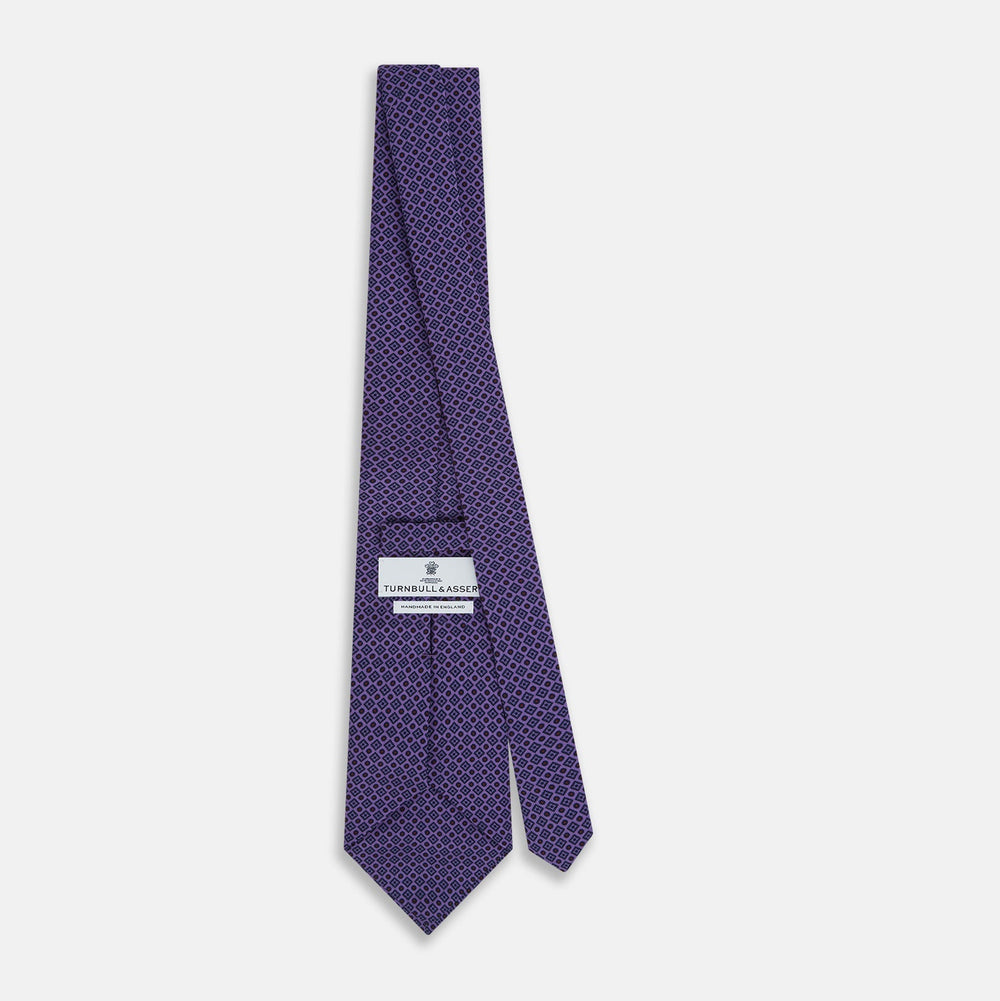 The Turnbull & Asser Purple Square and Circle Silk Tie is crafted from fine English silk, showcasing a purple design with a repeating geometric pattern of squares and circles for a refined, elegant look.