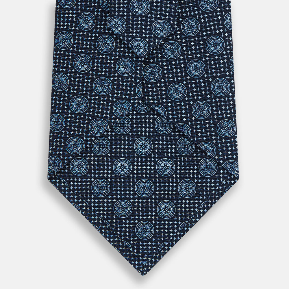 The Turnbull & Asser Navy Medallion Silk Tie features a rolled-up navy silk design with light blue circular medallions and small cross motifs.