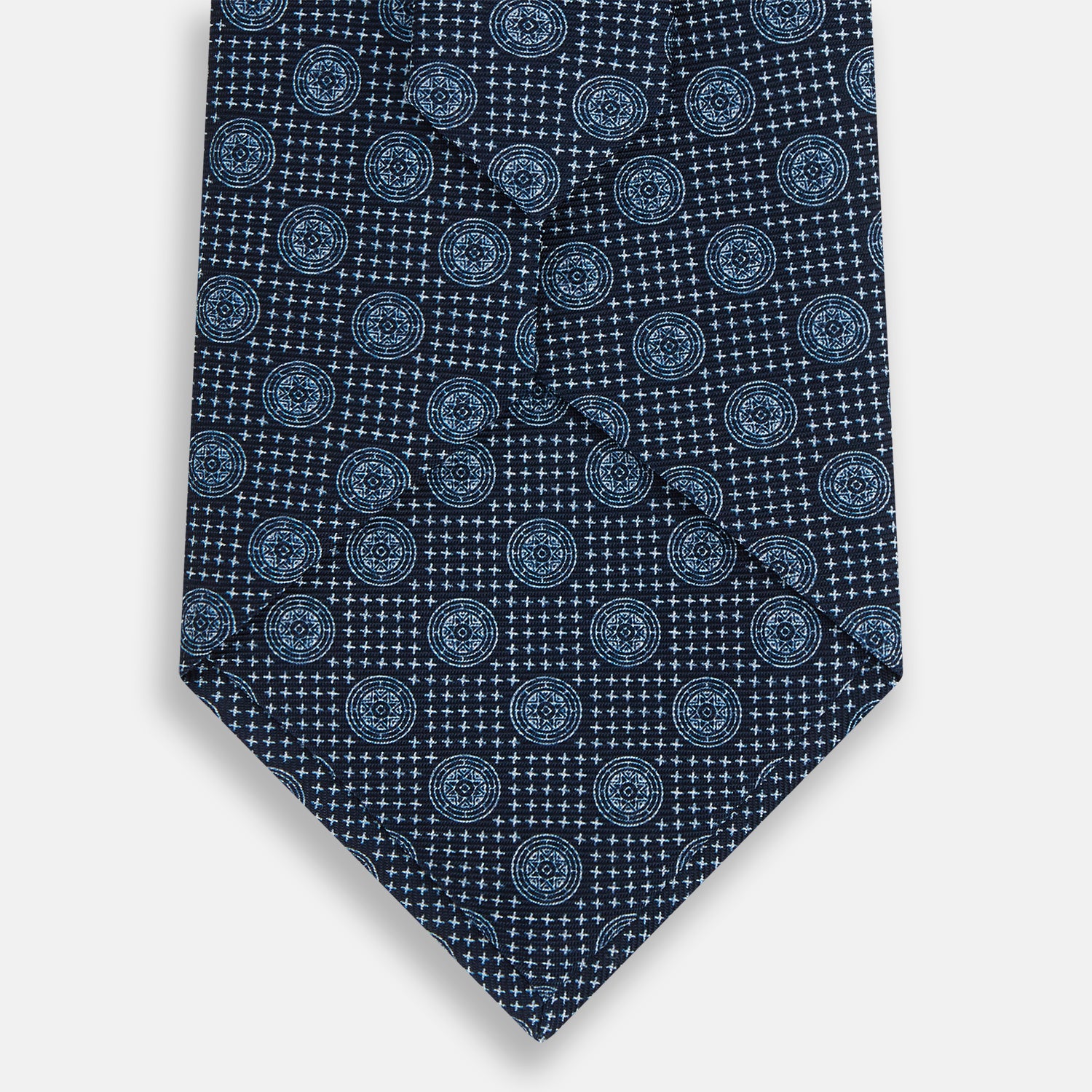 View 3 of product The Turnbull & Asser Navy Medallion Silk Tie features a rolled-up navy silk design with light blue circular medallions and small cross motifs.