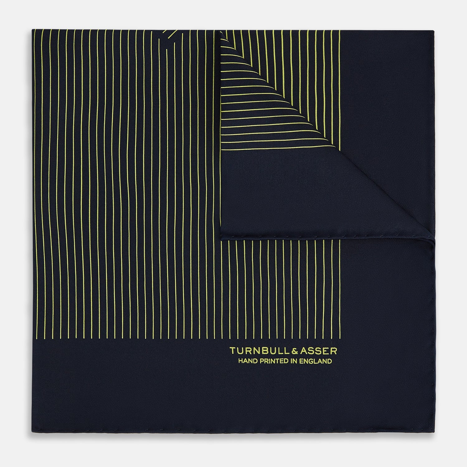 View 1 of product The Turnbull & Asser Navy and Gold Stripe Silk Pocket Square features light yellow vertical stripes, a folded corner, and "TURNBULL & ASSER HAND PRINTED IN ENGLAND" in gold at the bottom right.