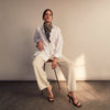 View 7 of product A woman with straight brown hair pulled back wears the Turnbull & Asser White Cotton Marlene Shirt, featuring classic menswear details, paired with high-waisted cream trousers against a neutral background.