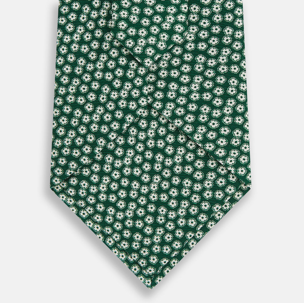 The Turnbull & Asser Forest Green Flower Patterned Silk Tie, crafted from fine English silk, features a repeating white floral design and is shown rolled up on a white background.