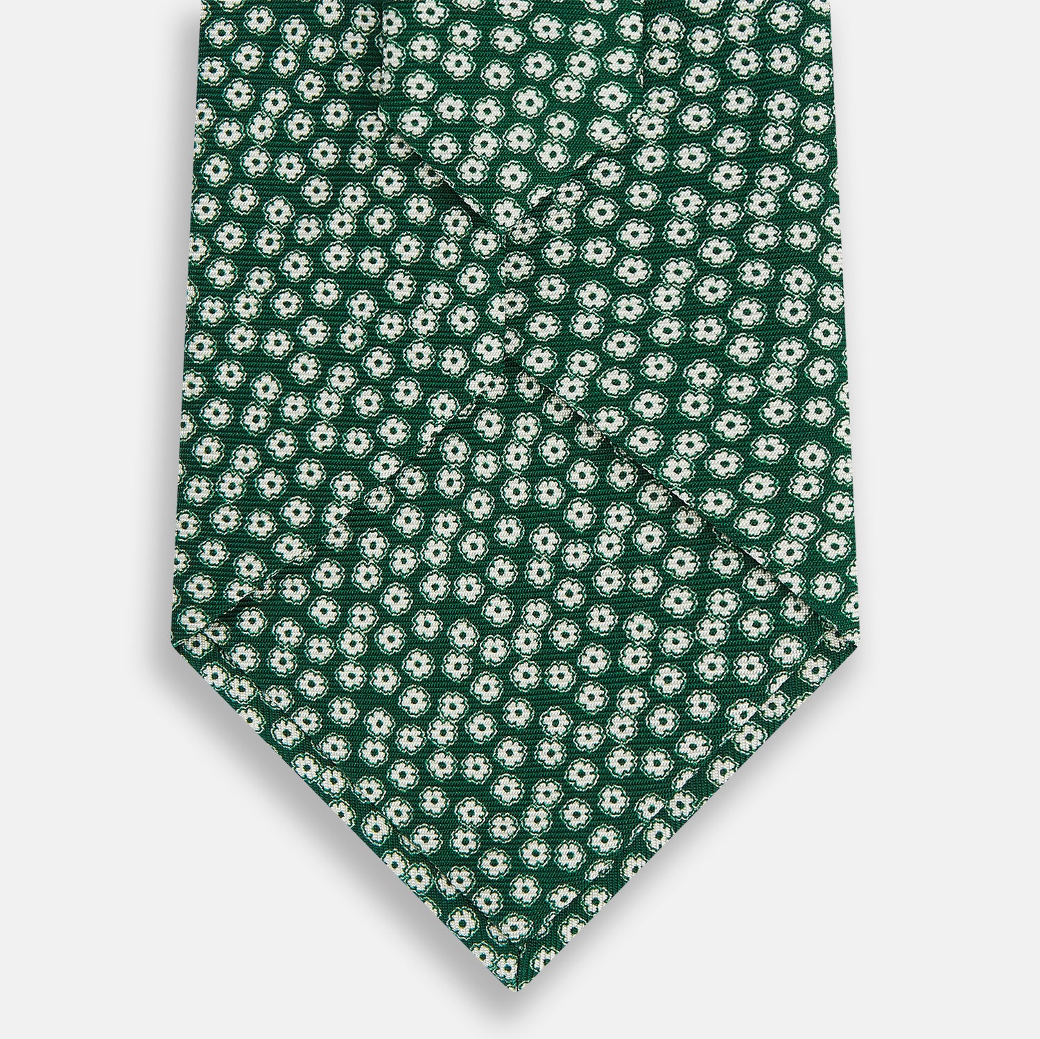 View 3 of product The Turnbull & Asser Forest Green Flower Patterned Silk Tie, crafted from fine English silk, features a repeating white floral design and is shown rolled up on a white background.