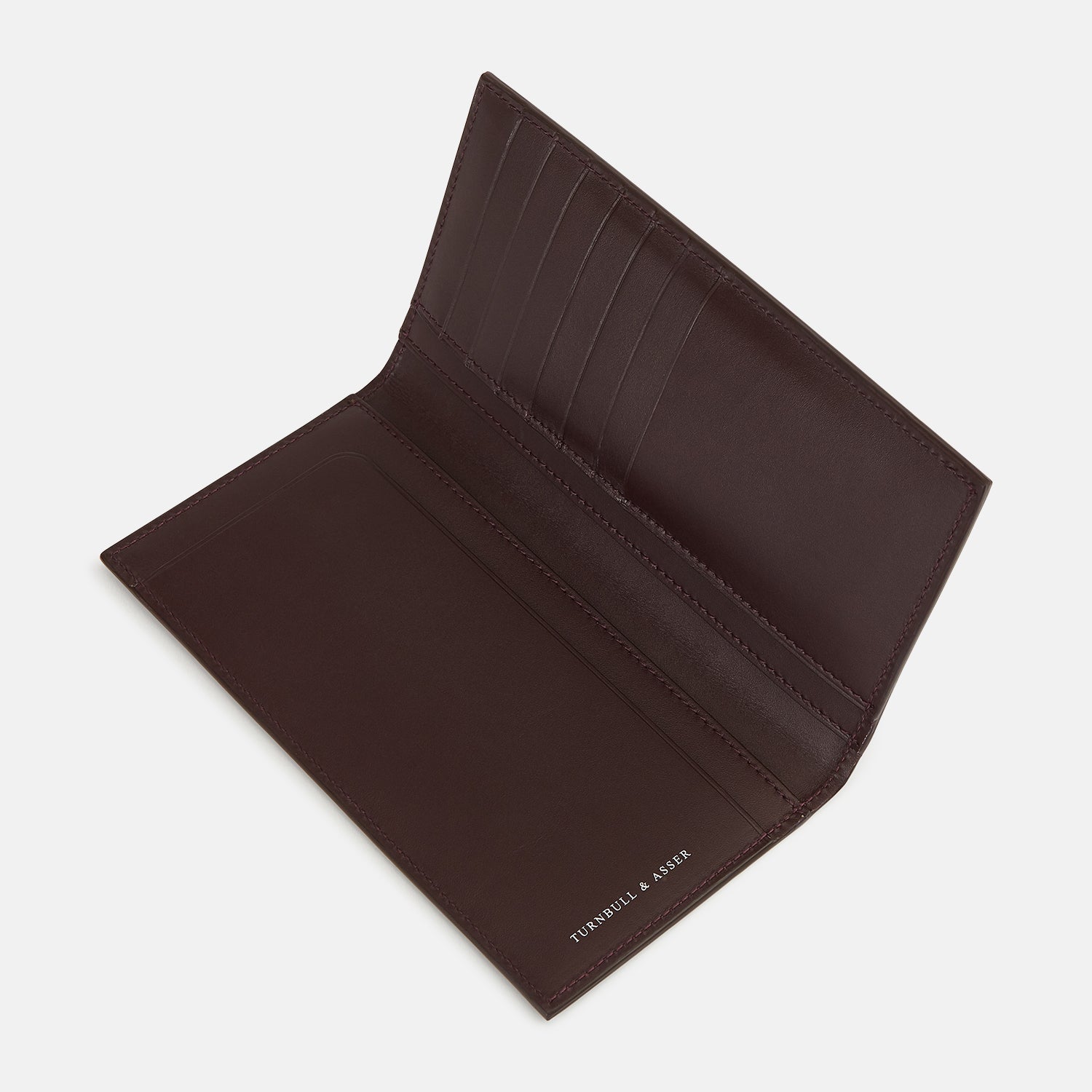 Image 3 of product The Turnbull & Asser Burgundy B Cut Continental Wallet, with smooth, unadorned surfaces and visible edge stitching, is pictured closed in rich burgundy Italian leather against a white background.