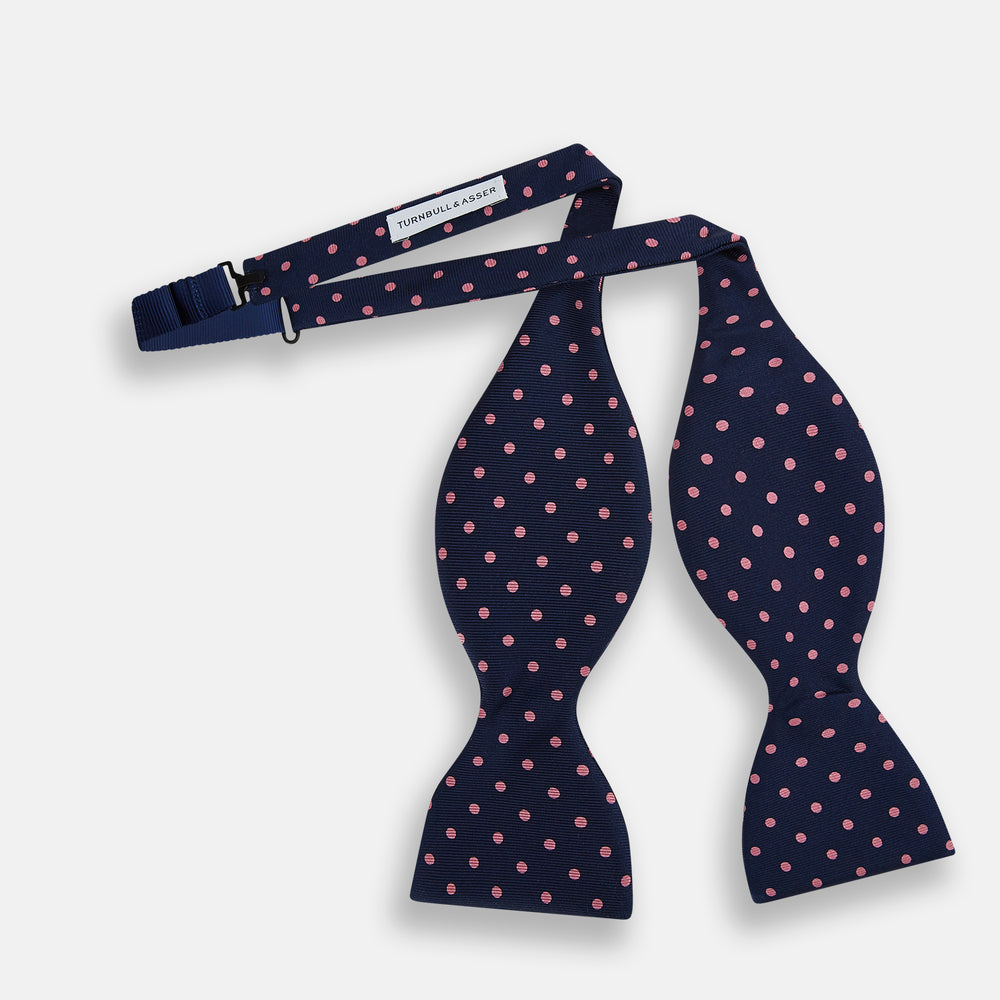 The Navy and Pink Spot Silk Bow Tie by Turnbull & Asser features evenly spaced pink polka dots on navy silk, shown against a plain white background.