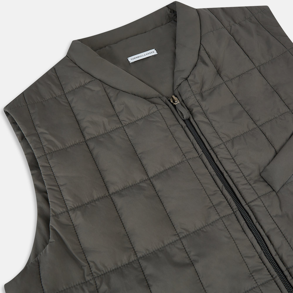 The Shadow Grey Quilted Gilet by Turnbull & Asser is a sleeveless, lightweight layer featuring a front zipper, two zippered side pockets, one chest pocket, and a rounded hem—shown on a plain white background.