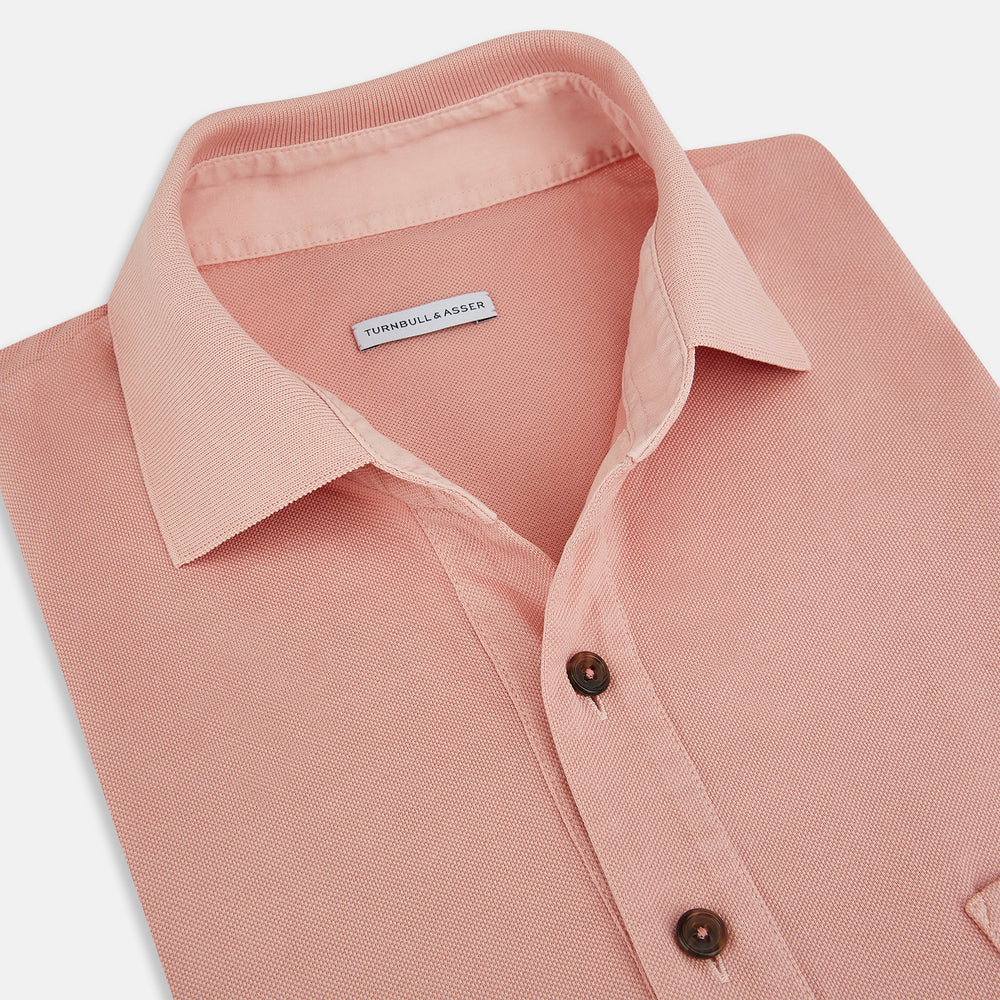 The Orange Polo Shirt by Turnbull & Asser features short sleeves, a collar, three-button placket, and a small buttoned chest pocket in soft cotton jersey—timeless men's style laid flat on a white background.