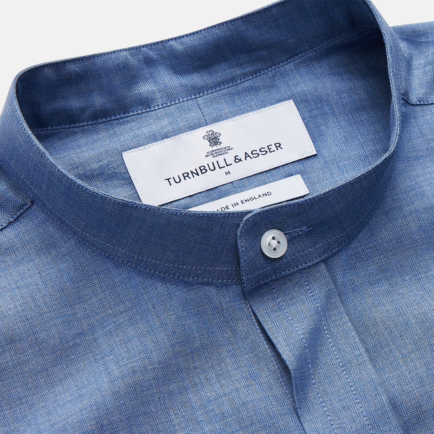 View 4 of product The Turnbull & Asser Blue Cotton Weekend Fit Blake Shirt features a light blue color, long sleeves, stand collar, white buttons, and a curved hem—ideal for casual weekends. Laid flat on a white background.