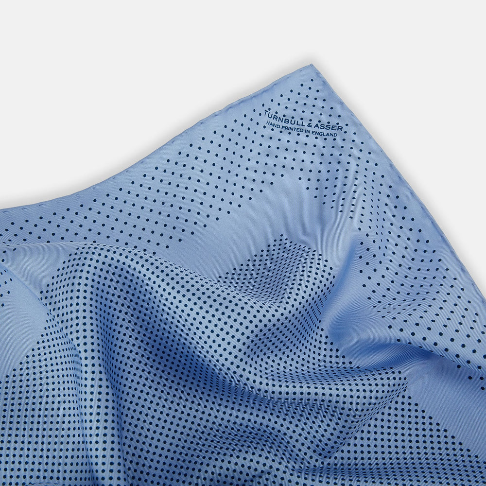 The Turnbull & Asser Pale Blue Dot Silk Pocket Square features pure silk in pale blue with a border and scattered small navy polka dots, neatly folded with one corner turned down.