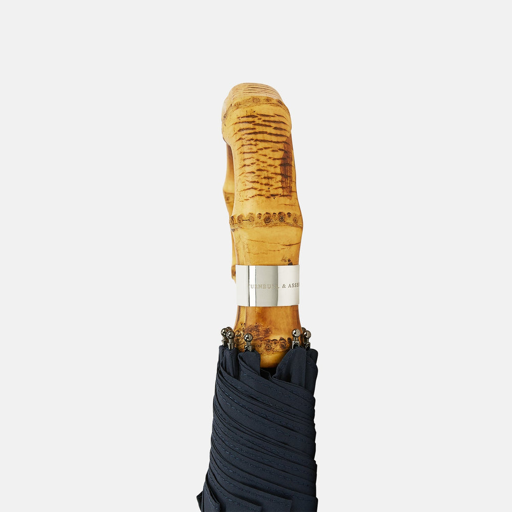 The Turnbull & Asser Navy Telescopic Umbrella with Whangee Crook Handle, featuring a silver shaft, is a refined men's accessory, shown open against a plain white background.