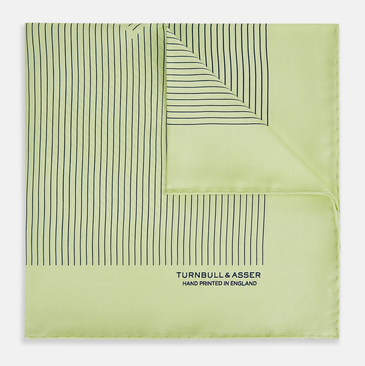 View 1 of product The Melon Green Stripe Silk Pocket Square by Turnbull & Asser features thin vertical black lines on light green silk, neatly folded to display both sides. The lower corner reads “TURNBULL & ASSER HAND PRINTED IN ENGLAND.”.