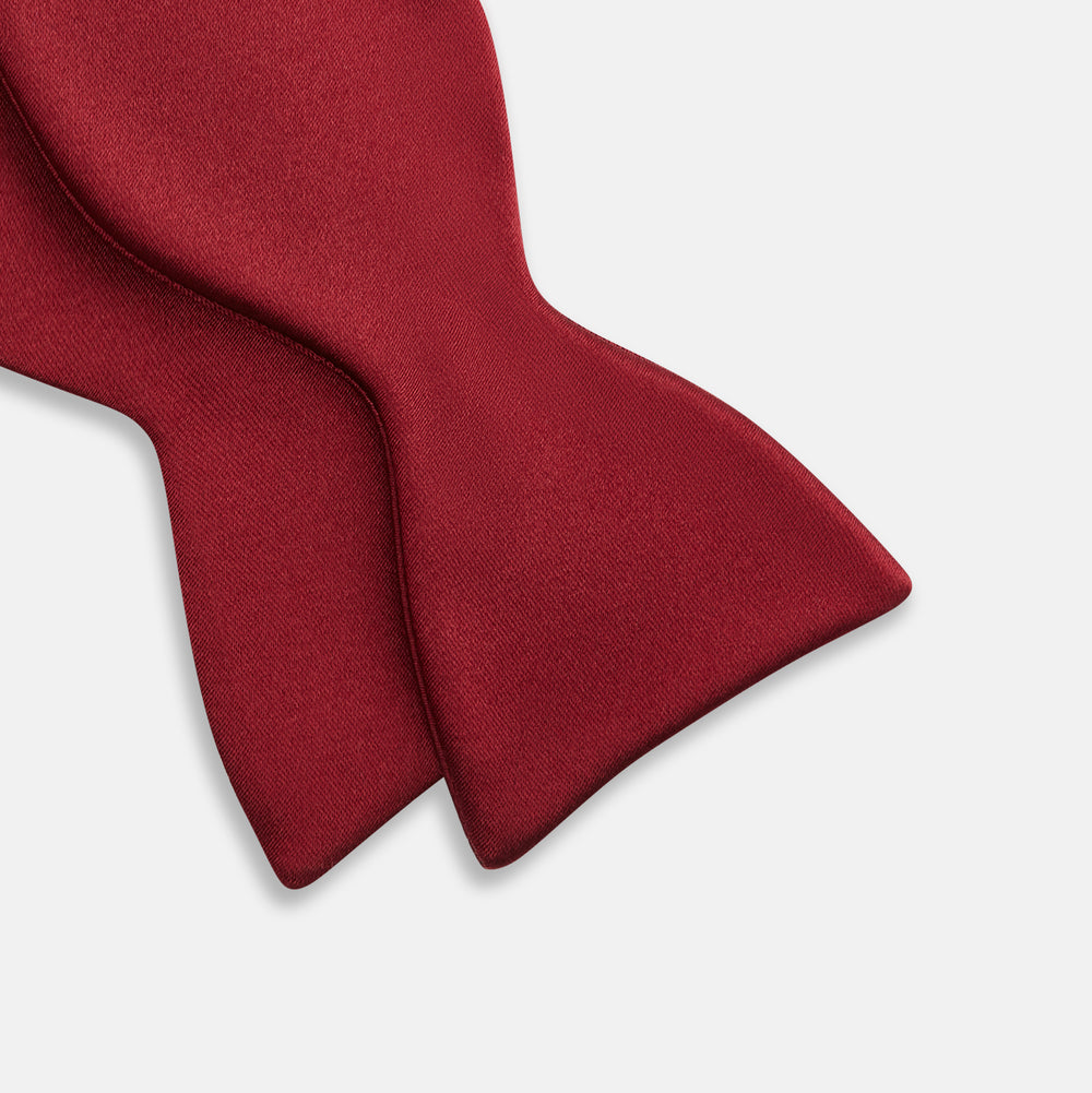 The Turnbull & Asser BURGUNDY SATIN BOW TIE features a deep red, smooth, and shiny finish—an essential accessory—neatly tied and showcased against a plain white background.