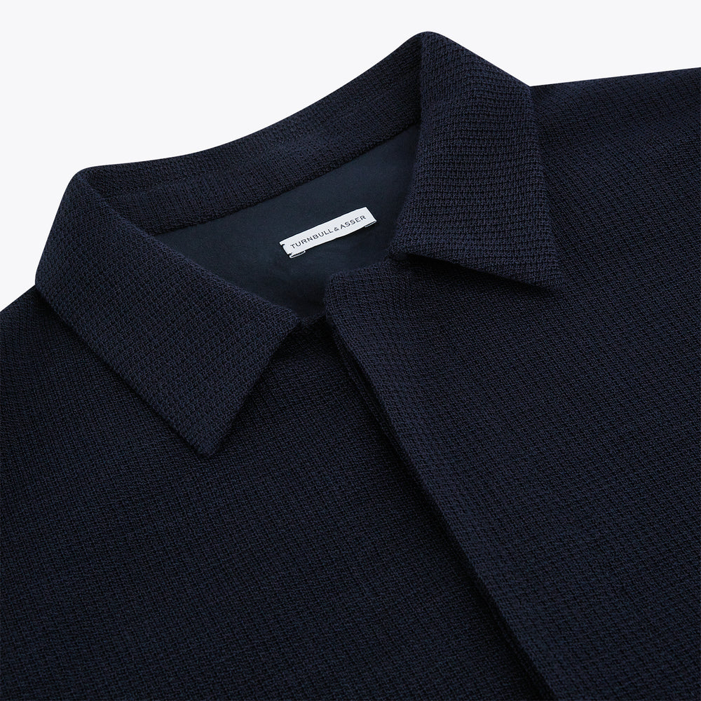 The Turnbull & Asser Navy Greenwich Knitted Overshirt, made from Italian wool with a collar, two front flap pockets, and a hidden button placket, is shown laid flat on a white background.