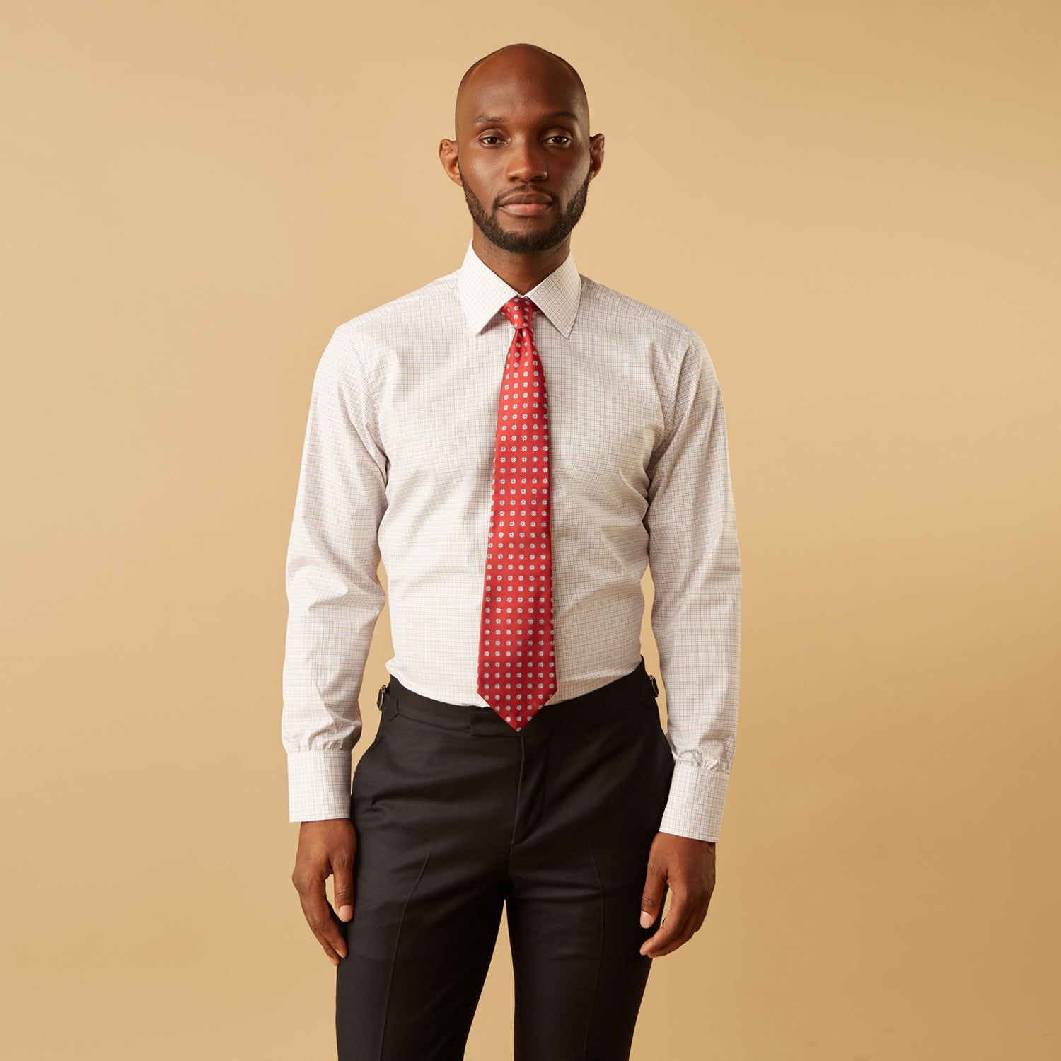 View 1 of product A man stands against a beige background, facing forward with a neutral expression and arms relaxed, wearing the Turnbull & Asser Red Multi Check Regular Fit Mayfair Shirt.