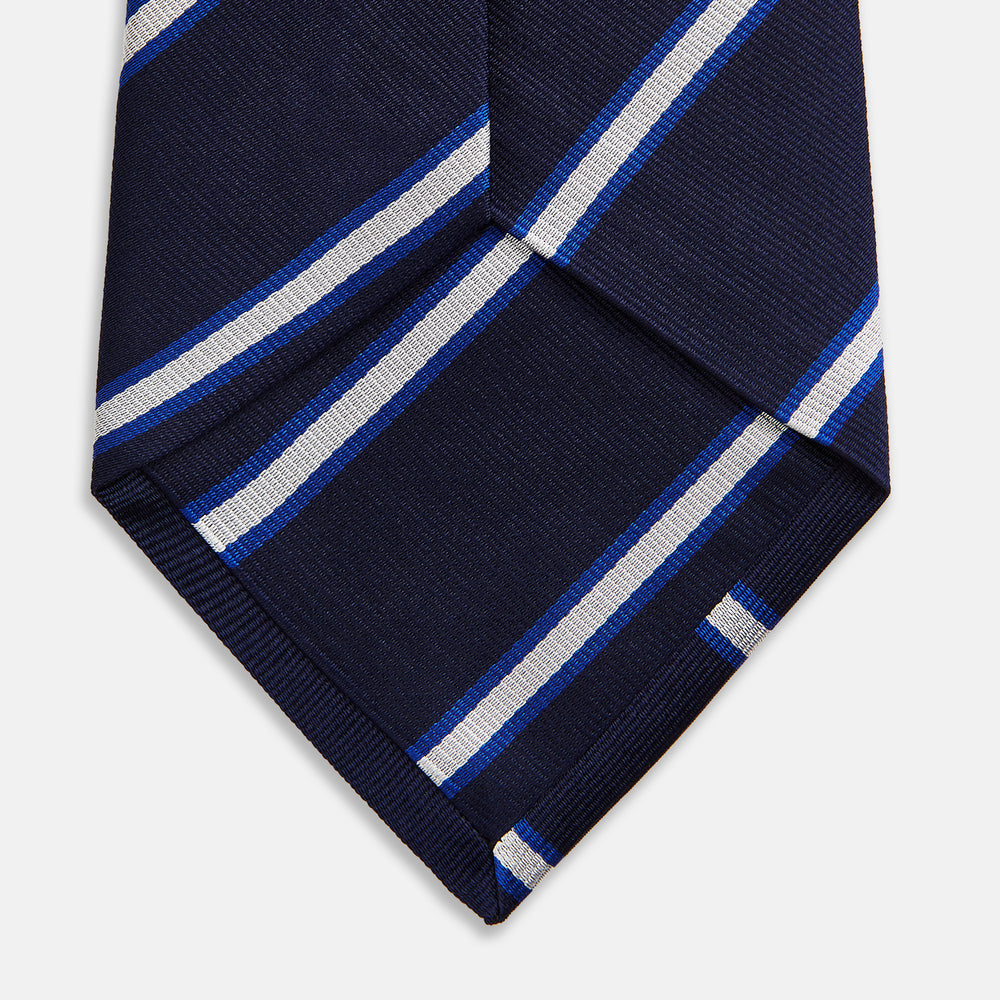 The White and Navy Blazer Silk Tie by Turnbull & Asser features diagonal white and light blue stripes on navy silk, shown rolled on a white background. A refined choice to complement any office shirt.