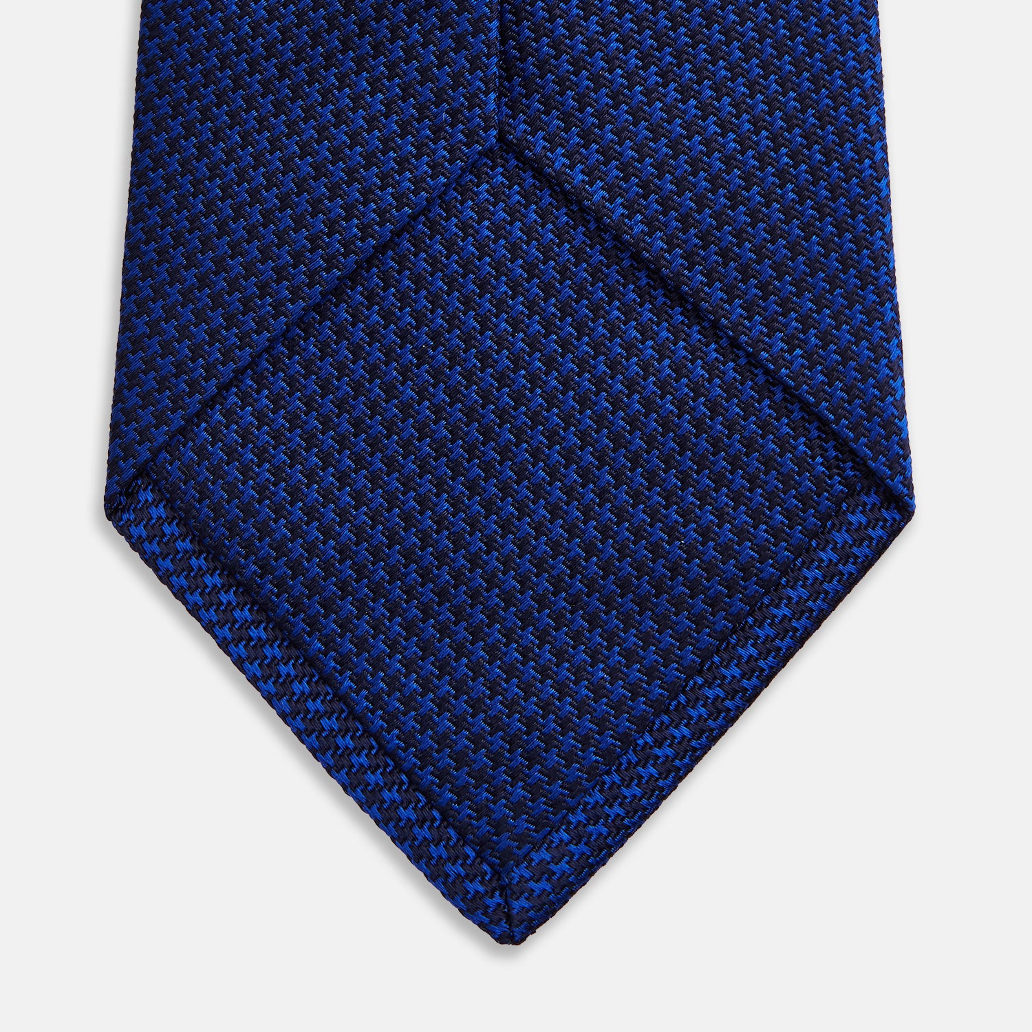 View 4 of product The HOUNDSTOOTH NAVY CRUISE TIE by Turnbull & Asser, featuring a textured blue design, is displayed rolled-up on a plain white background—an essential accessory for elevating formal looks.