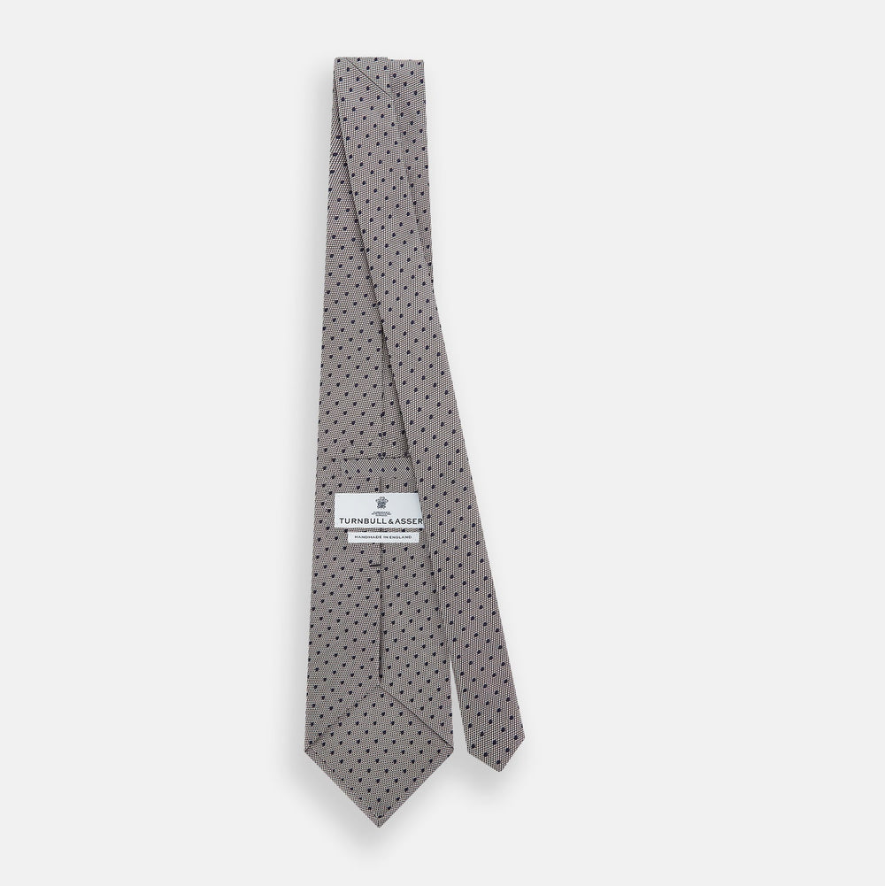 The Turnbull & Asser Navy and Lilac Micro Dot Silk Tie is shown rolled up on a white background, featuring a refined pattern of small lilac dots on navy silk.