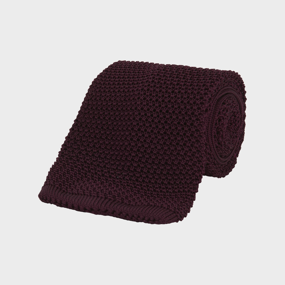 The Turnbull & Asser MTIE011-ZAI003 TIES 7.5CM is a plain burgundy tie shown rolled on a white background, featuring straight edges and textured knit—ideal for the modern gentleman’s versatile wardrobe.