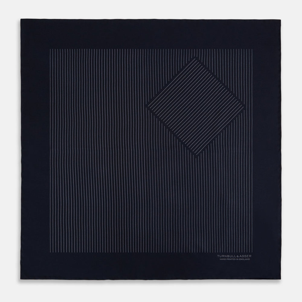 The Navy and Charcoal Stripe Silk Pocket Square by Turnbull & Asser features fine hand-rolled edges, thin white stripes on navy, and TURNBULL & ASSER HAND PRINTED IN ENGLAND in white on the corner.