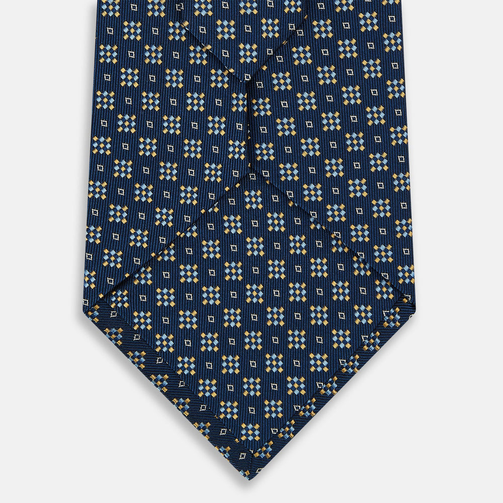 The Turnbull & Asser Navy Diamond Silk Tie features a diamond pattern of small white and yellow squares, embodying British craftsmanship, shown on a plain white background.