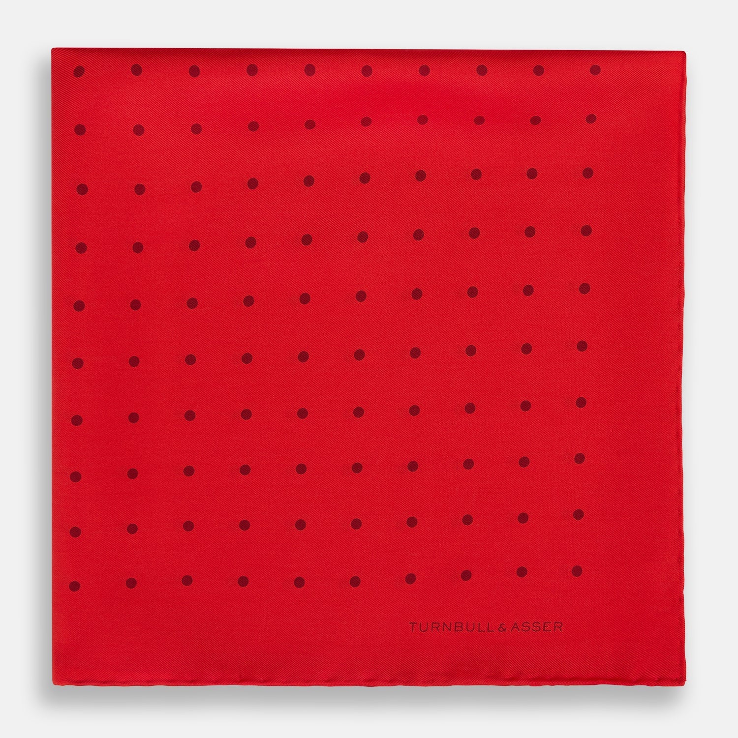 View 3 of product The Turnbull & Asser Red and Burgundy Spot Silk Pocket Square features evenly spaced small spots and the brand logo in the bottom right corner—perfect for formal wear. One corner is folded to show the reverse side.