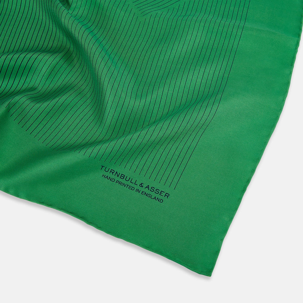 The Hunter Green Stripe Silk Pocket Square by Turnbull & Asser features thin black vertical stripes on one corner and “Turnbull & Asser Hand Printed in England” printed in black, reflecting classic British heritage.