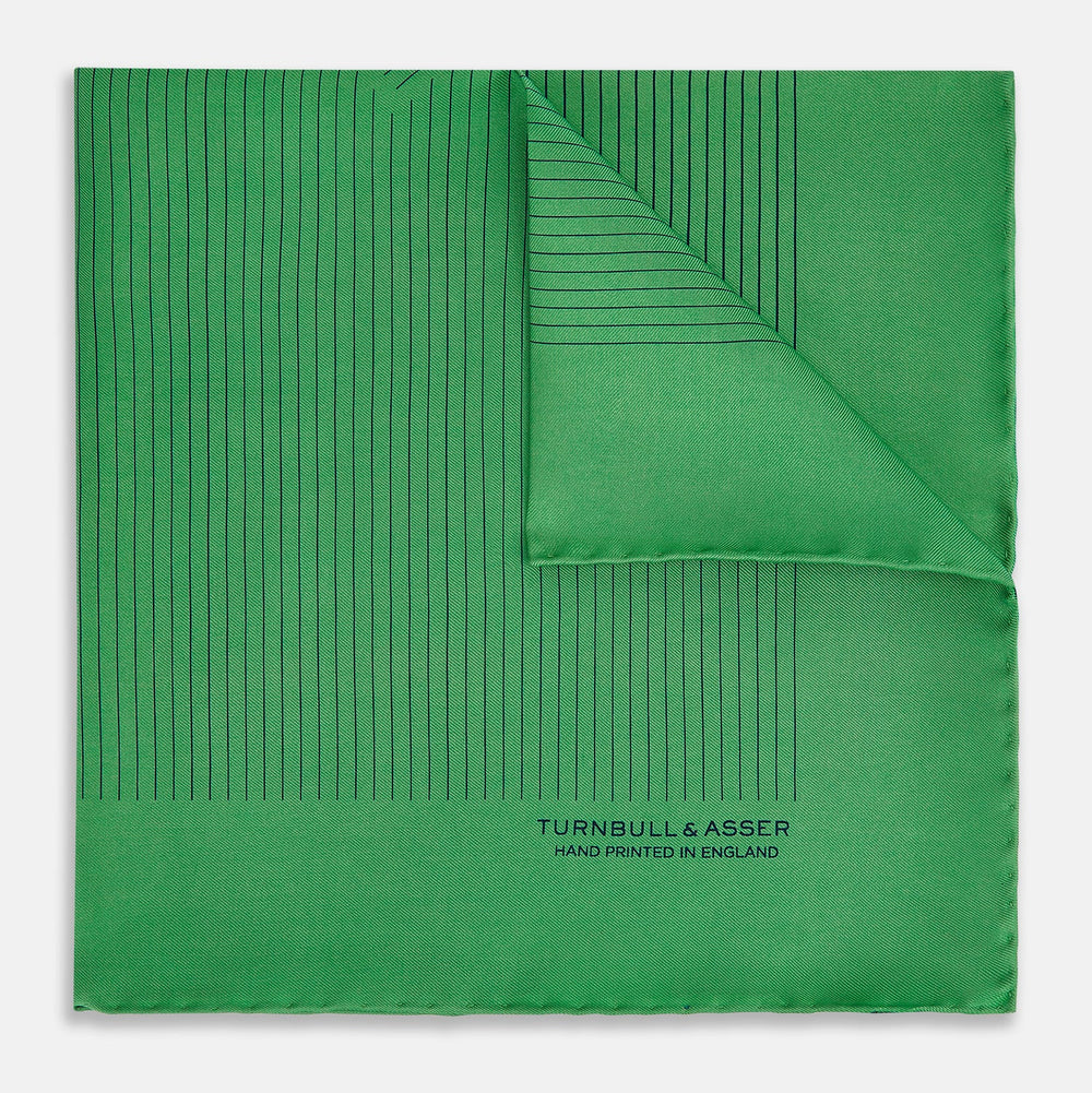 The Hunter Green Stripe Silk Pocket Square by Turnbull & Asser features thin black vertical stripes on one corner and “Turnbull & Asser Hand Printed in England” printed in black, reflecting classic British heritage.