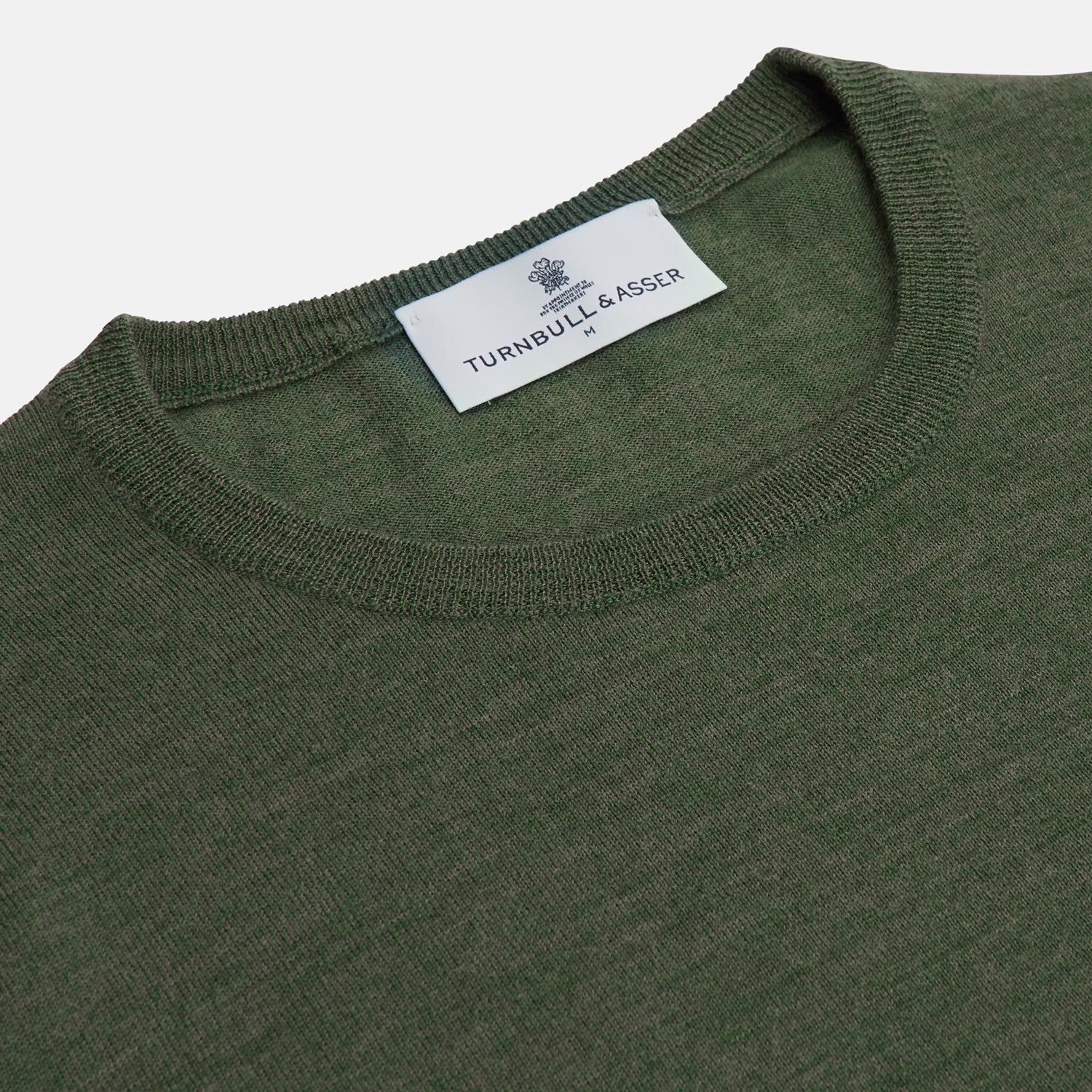 View 4 of product A man stands facing the camera against a plain light background, wearing the Turnbull & Asser Bottle Green Merino Kingston Crew Neck Jumper with dark pants and black shoes. His arms rest at his sides and he has a neutral expression.