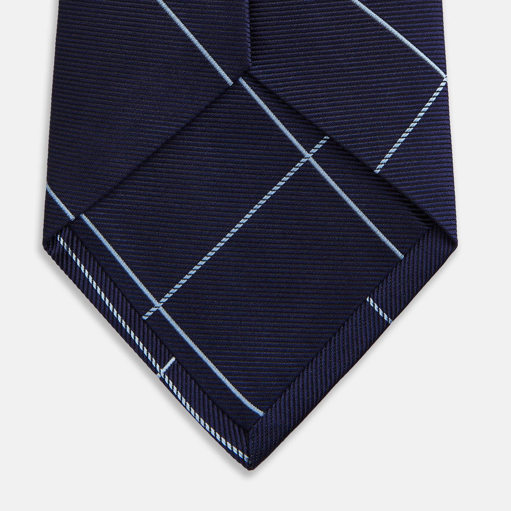 The Turnbull & Asser WINDOW PANE NAVY RIVER TIE features a navy blue base with a subtle light blue check pattern, elegantly rolled on a white background—a sophisticated men's accessory for any wardrobe.