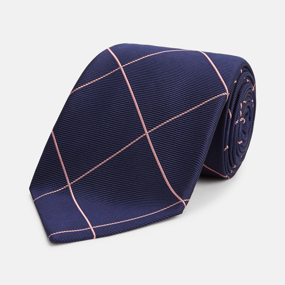 The Turnbull & Asser FONDANT PINK and WINDOW PANE NAVY Silk Tie features a subtle ribbed texture with a pink grid pattern on navy—an elegant choice for polished office attire, shown neatly rolled on a white background.