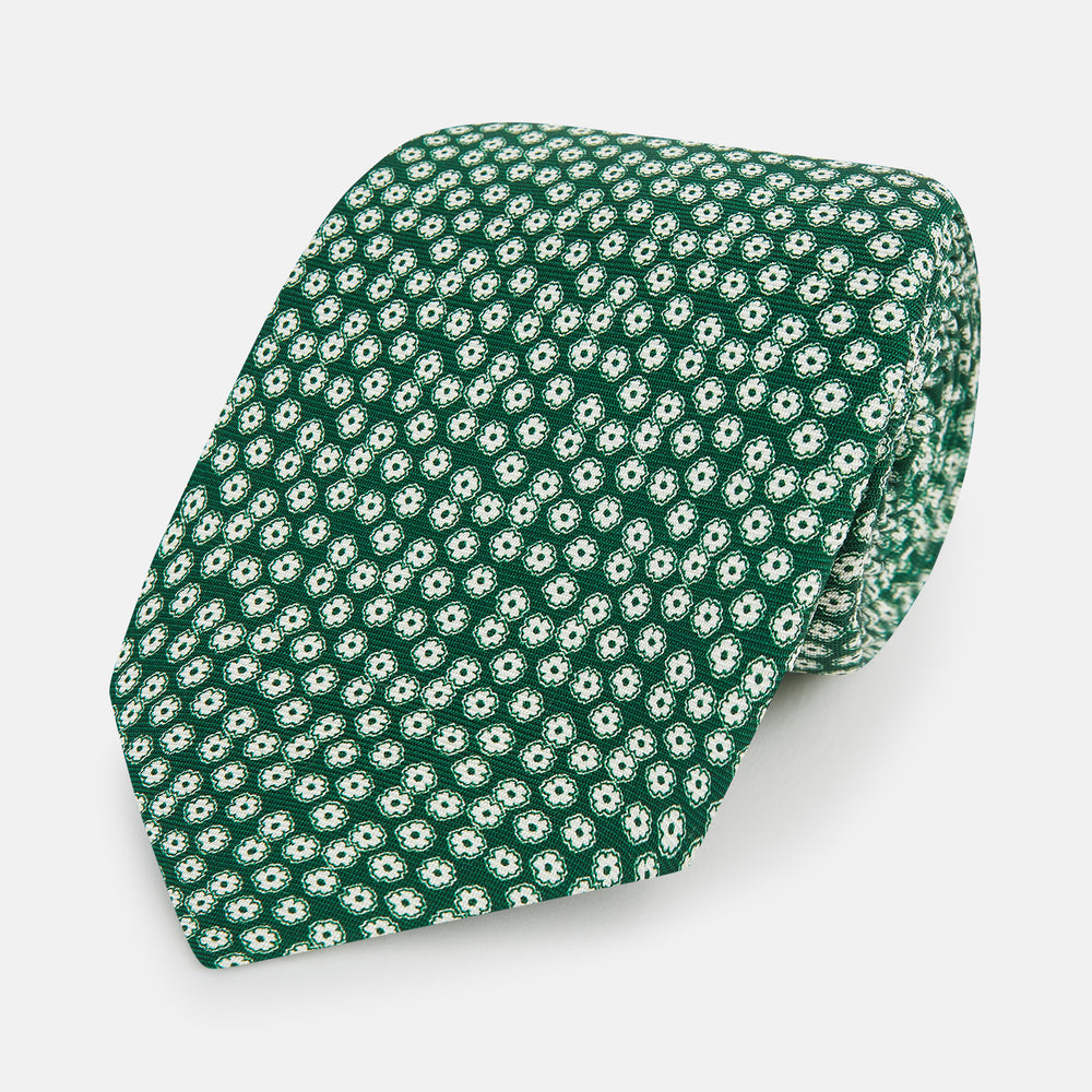 The Turnbull & Asser Forest Green Flower Patterned Silk Tie, crafted from fine English silk, features a repeating white floral design and is shown rolled up on a white background.