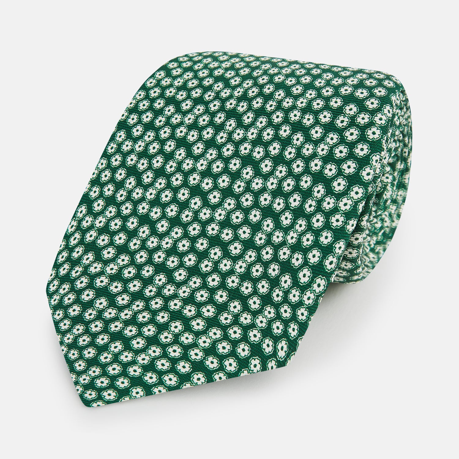 View 1 of product The Turnbull & Asser Forest Green Flower Patterned Silk Tie, crafted from fine English silk, features a repeating white floral design and is shown rolled up on a white background.