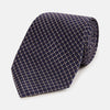 View 1 of product The Turnbull & Asser Silver and Navy Diamond Silk Tie features a neatly rolled silk design with a diagonal grid of small, light squares and lines, displayed on a plain background—perfect for an elegant, professional look.