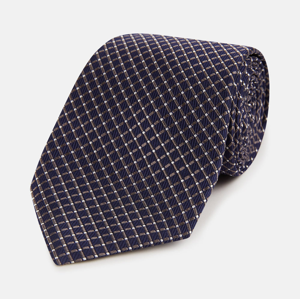 The Turnbull & Asser Silver and Navy Diamond Silk Tie features a neatly rolled silk design with a diagonal grid of small, light squares and lines, displayed on a plain background—perfect for an elegant, professional look.