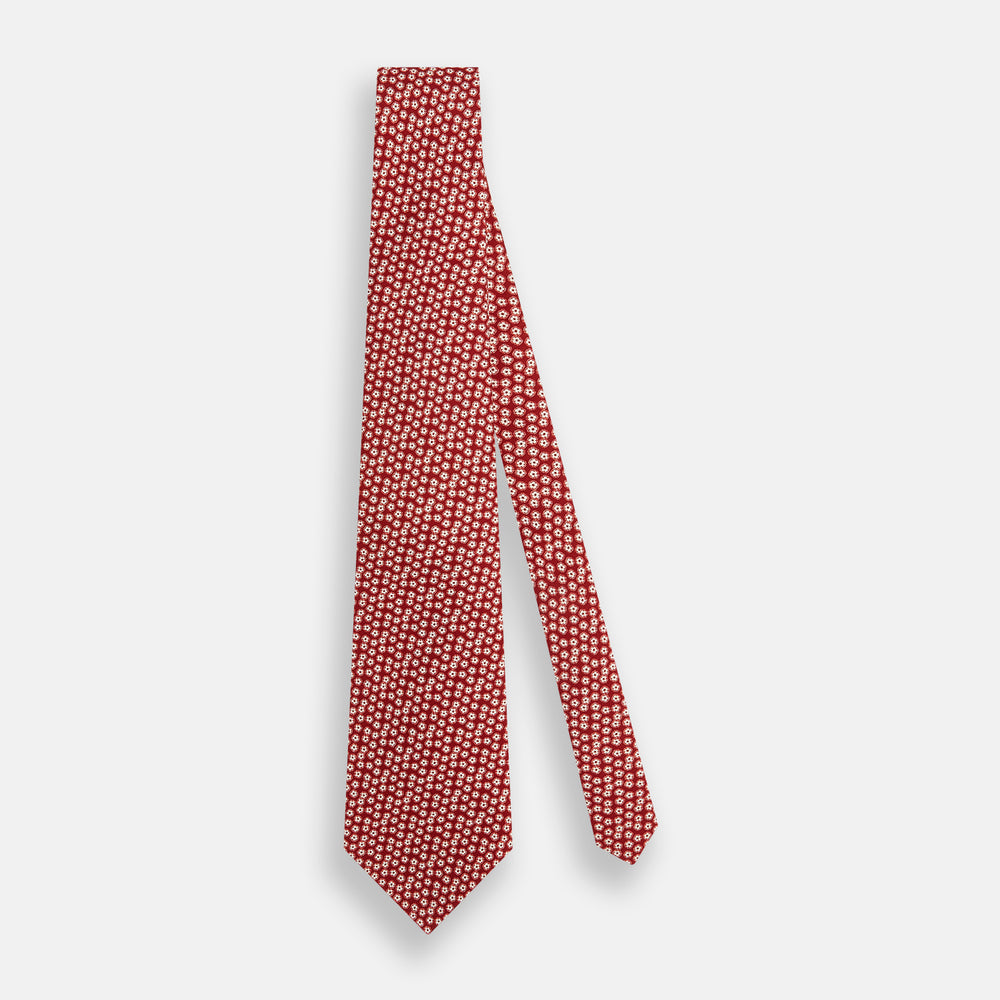 The Turnbull & Asser Red Flower-Patterned Printed Silk Tie, made from fine English silk, features a repeating white floral design and is shown rolled on a plain white background.