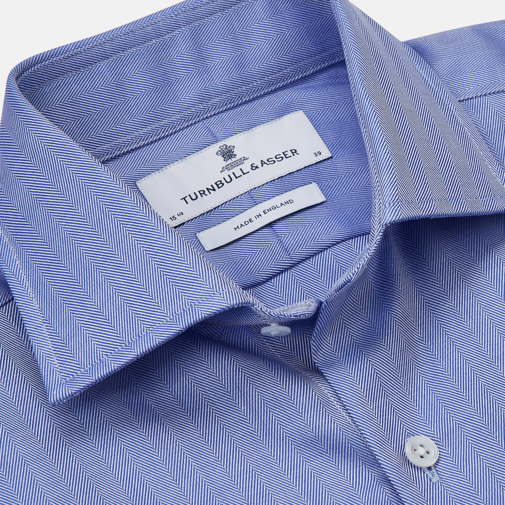Turnbull & Asser's Blue Herringbone Tailored Fit Shirt with a Kent collar and white buttons is shown laid flat on a white background.