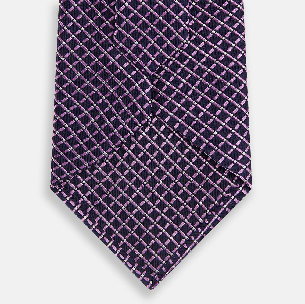 A rolled-up Turnbull & Asser Purple and Navy Diamond Silk Tie displays its elegant grid pattern of light pink and white lines on a white background.