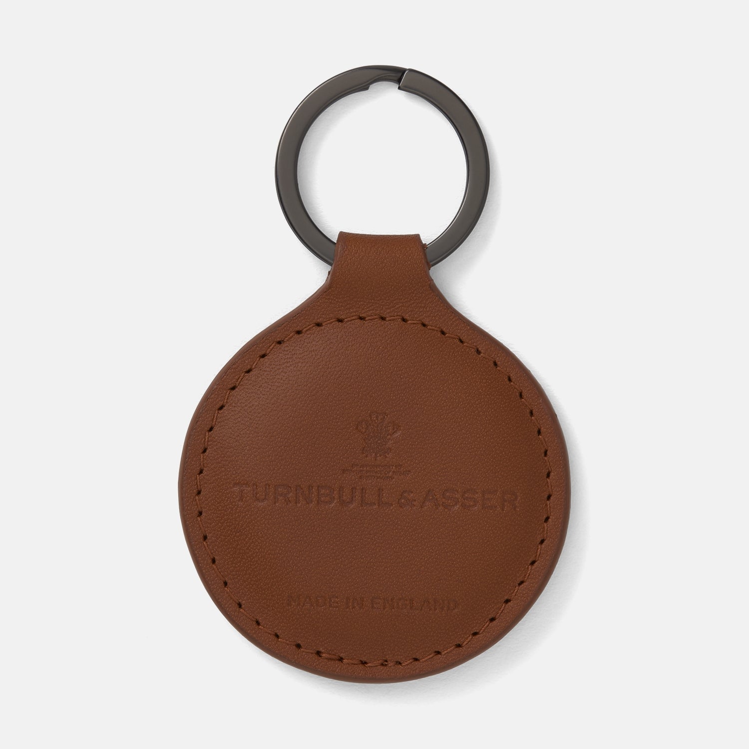 View 1 of product A tan circular leather fob holder by Turnbull & Asser, featuring visible stitching, embossed branding, and 'Made in England,' attached to a metal key ring.