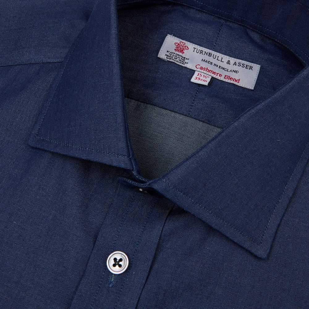 The Turnbull & Asser Dark Blue Denim-Cashmere Shirt features a Regent collar, long sleeves, and 3-button cuffs, neatly folded and displayed on a plain light background.