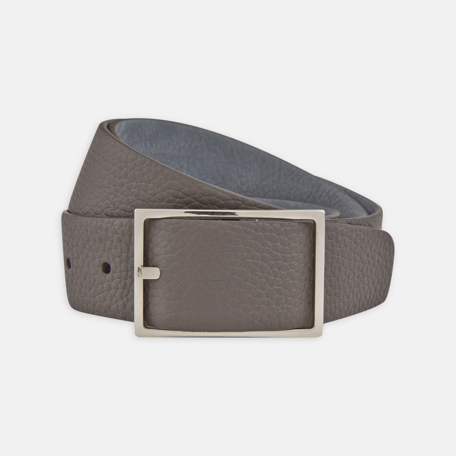 View 1 of product The Turnbull & Asser Nubuk Reversible Leather Belt is shown coiled on a plain white background, featuring gray textured leather and a rectangular silver buckle.