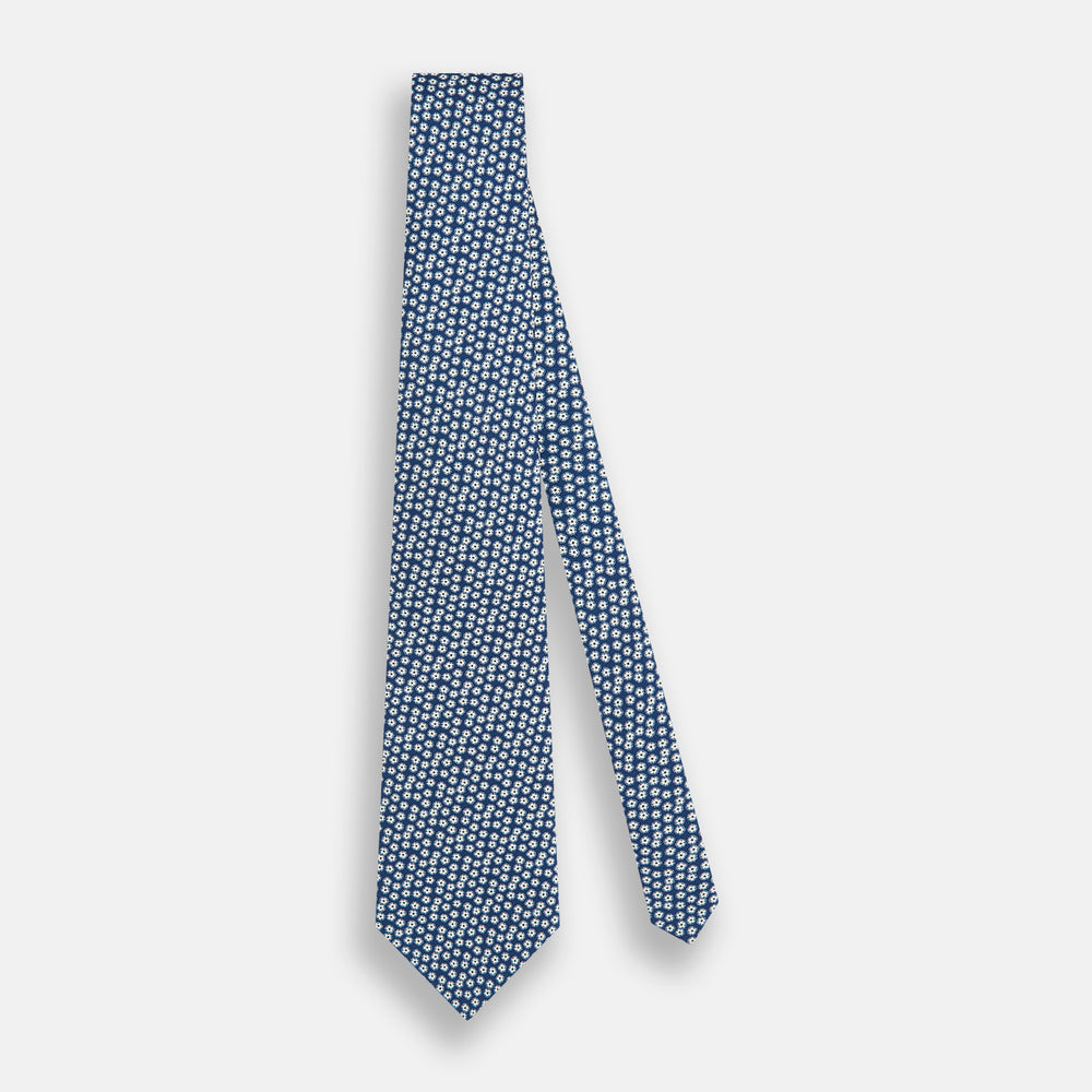 The Turnbull & Asser Azzurro Flower Patterned Silk Tie features a repeating motif of small white flowers with dark centers on blue silk, rolled up and displayed against a plain white background.